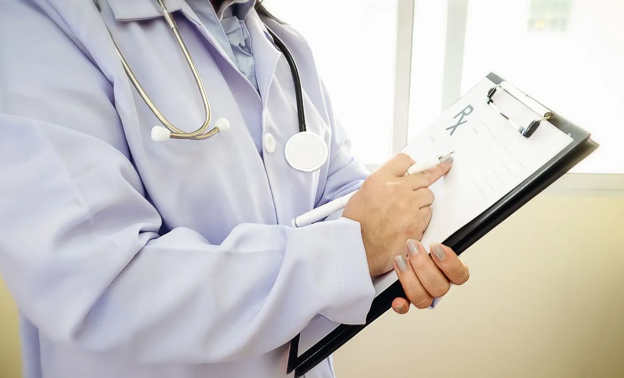 Médico preenchendo prontuário com estetoscópio sobre a mesa